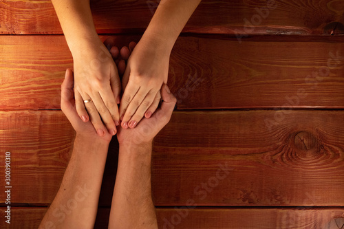 Men's and women's hands. Wife put her hands on her husband's palms on background of a red textured wooden table. Concept of family relations, help, kindness, understanding, thanksgiving and love.