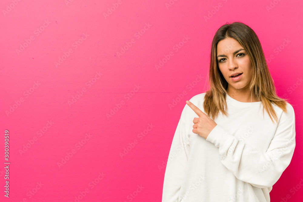 Young authentic charismatic real people woman against a wall smiling and pointing aside, showing something at blank space. Young authentic charismatic real people woman against a wall smiling and pointing aside, showing something at blank space.