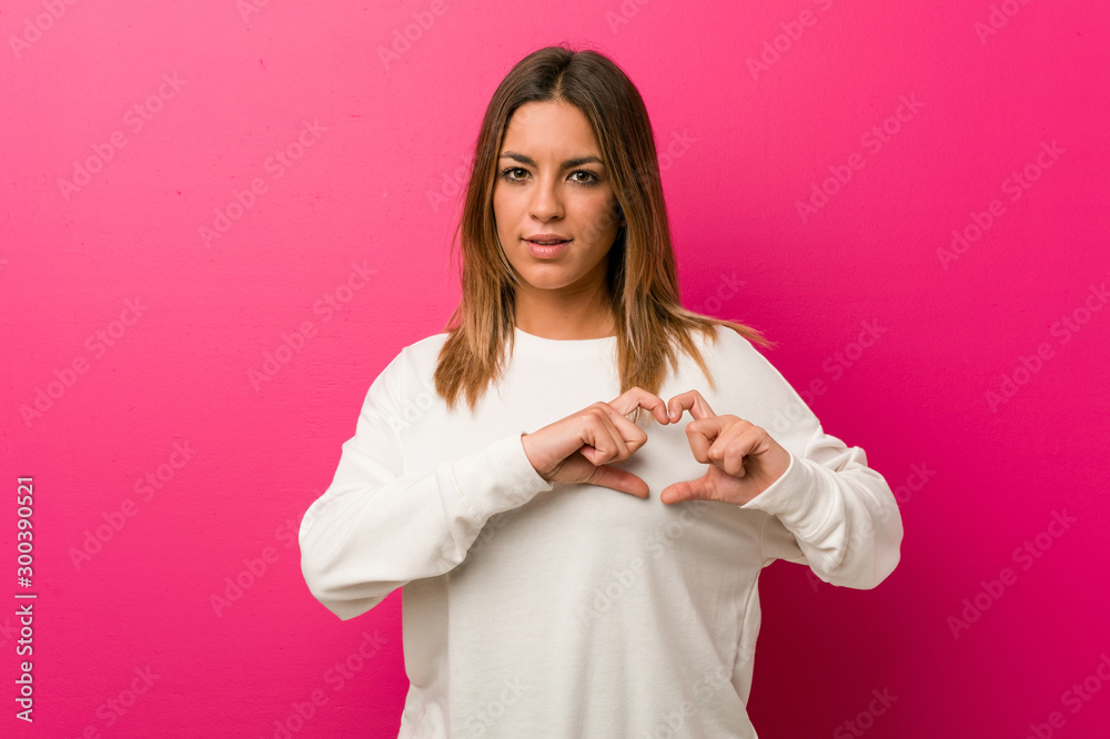 Young authentic charismatic real people woman against a wall smiling and showing a heart shape with hands. Young authentic charismatic real people woman against a wall smiling and showing a heart shape with hands.