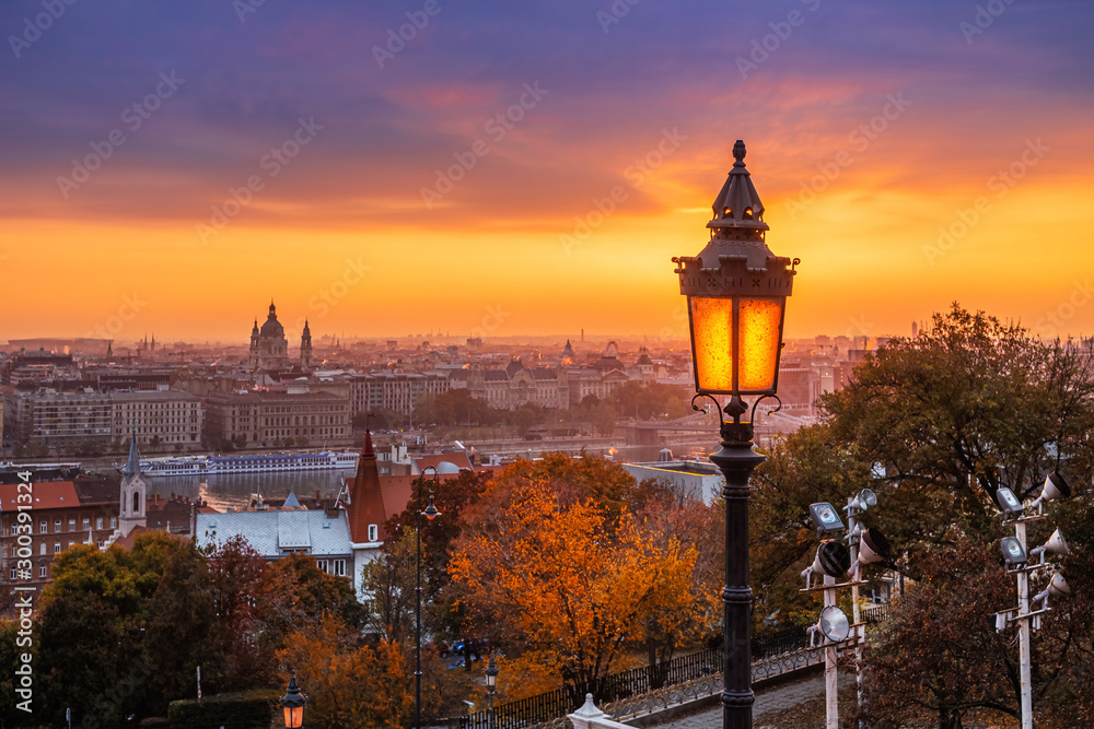 Budapest, Hungary - Colorful autumn morning at Budapest. Street lamp at the Fisherman's Bastion, St. Stephen's Basilica and amazing golden sunrise at the background with autumn foliage and trees