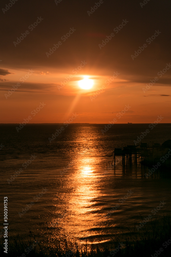 Coucher de soleil doré sur l'océan alors que des cabanes de pêcheurs se distinguent