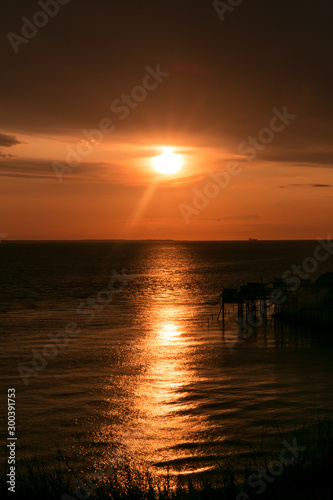 Coucher de soleil doré sur l'océan alors que des cabanes de pêcheurs se distinguent © LeaEmilie
