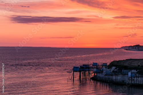 Cabanes de pêcheurs au dessus de l'océan sous un coucher de soleil enflammant le ciel de rose