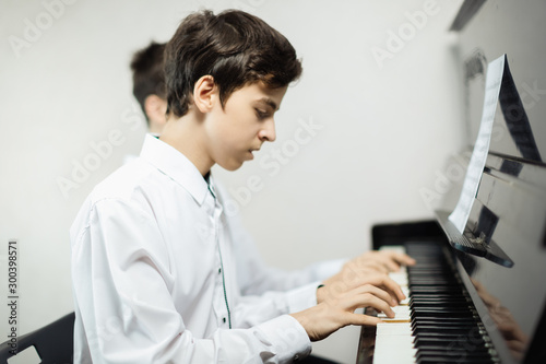 After school, the boy relaxes at home playing a piano. The hands of the guy are beautifully lying on the keys of the old piano and play a familiar melody