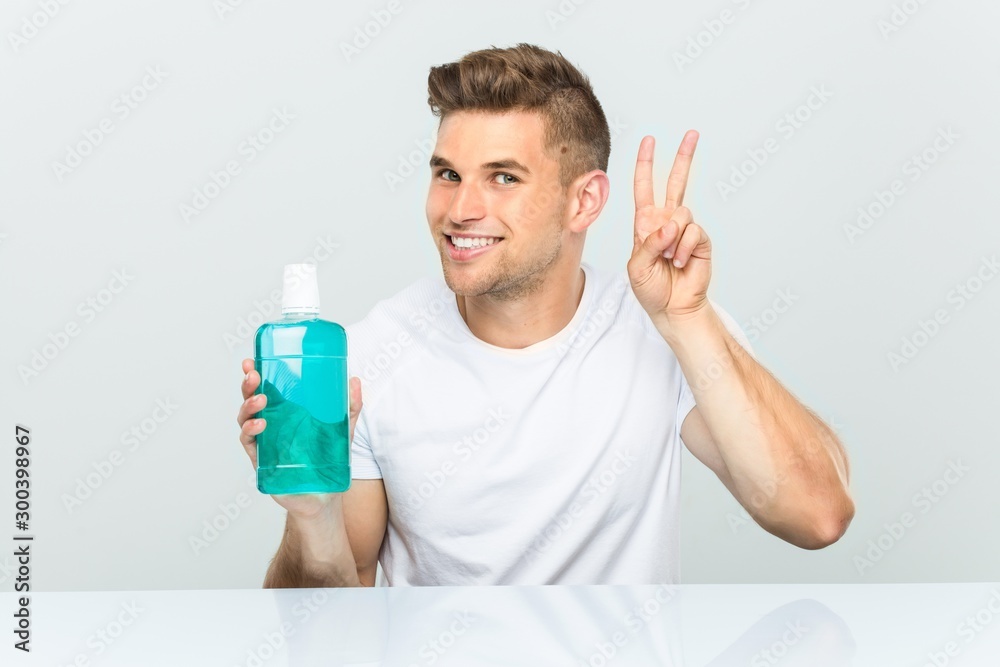 Young man holding a mouthwash showing victory sign and smiling broadly. Young man holding a mouthwash showing victory sign and smiling broadly.