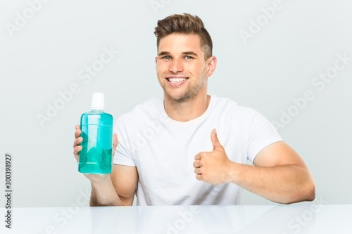 Young man holding a mouthwash smiling and raising thumb up