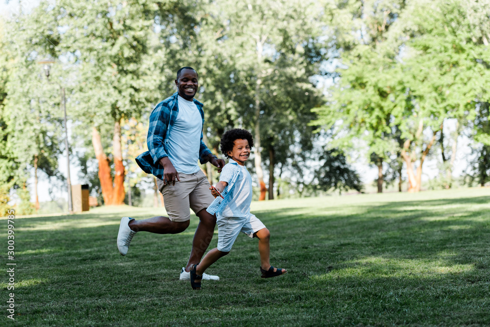 happy african american father and son running on grass happy african american father and son running on grass
