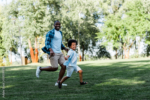 happy african american father and son running on grass