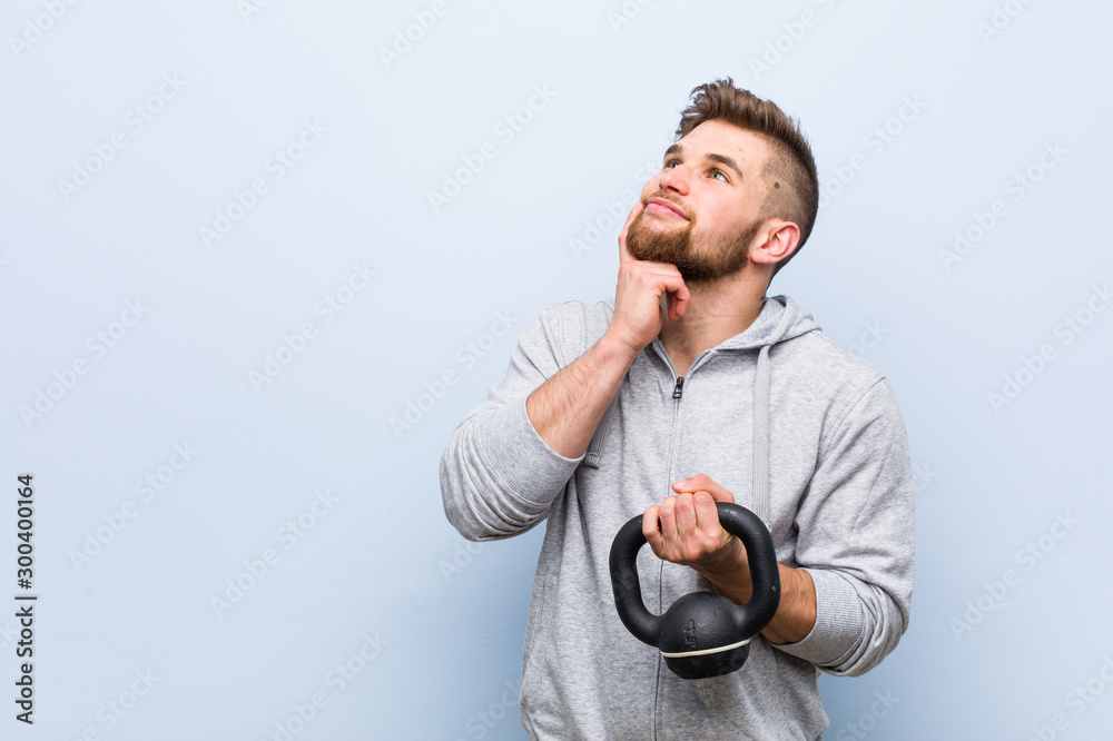 Young caucasian sportsman holding a dumbbell looking sideways with doubtful and skeptical expression. Young caucasian sportsman holding a dumbbell looking sideways with doubtful and skeptical expression.