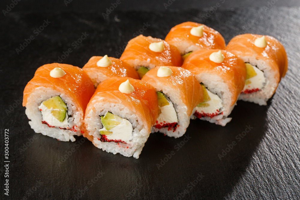 Sushi Rolls with salmon, avocado, flying fish caviar and Cream Cheese inside on black slate isolated. Philadelphia roll sushi with salmon. Sushi menu. Horizontal photo. Sushi Rolls with salmon, avocado, flying fish caviar and Cream Cheese inside on black slate isolated. Philadelphia roll sushi with salmon. Sushi menu. Horizontal photo.