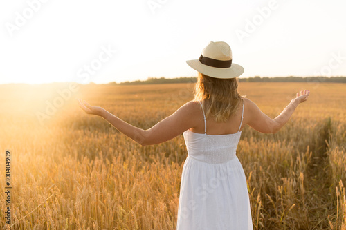 nature, people and happiness concept - happy young woman in white dress and straw hat and enjoying freedom on cereal field in summer