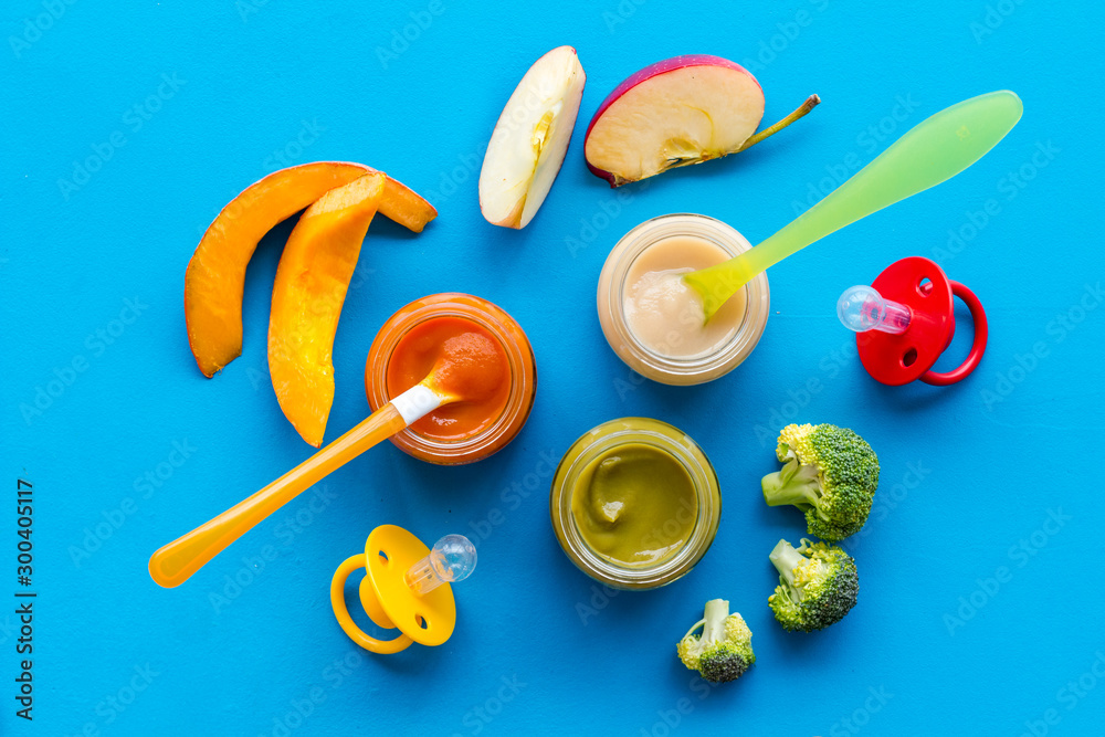 Baby food. Colorful puree in glass jars near vegetables and fruits on blue background top view Baby food. Colorful puree in glass jars near vegetables and fruits on blue background top view