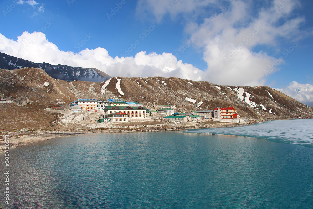 View of Gokyo village on the coast of Gokyo lake in Himalayas in Nepal. Mount Everest is hidden in white clouds in the background. Part of the lake is covered with ice.