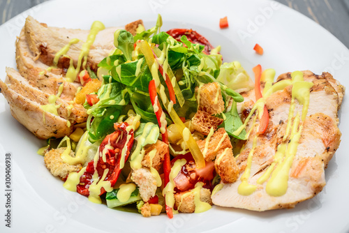 Caesar salad with croutons, quail eggs, cherry tomatoes and grilled chicken on a wooden background