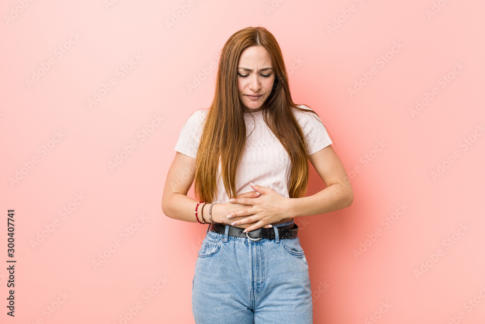 Young redhead ginger woman against a pink wall sick, suffering from stomachache, painful disease concept. Young redhead ginger woman against a pink wall sick, suffering from stomachache, painful disease concept.