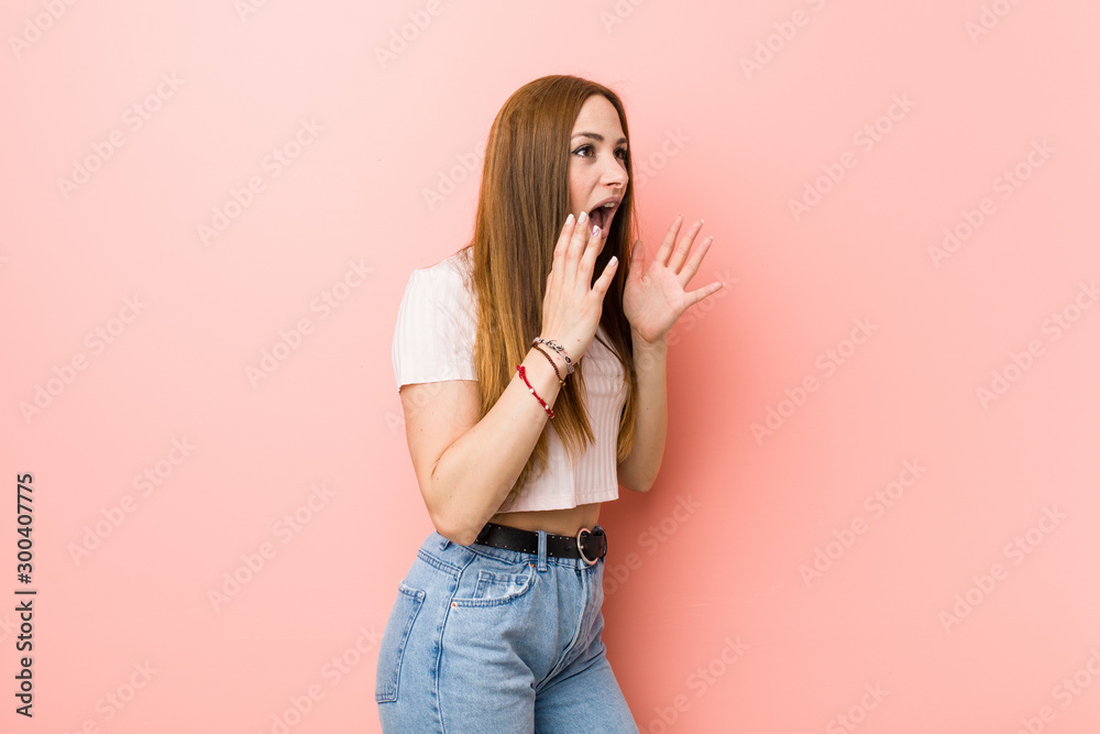 Young redhead ginger woman against a pink wall shouts loud, keeps eyes opened and hands tense. Young redhead ginger woman against a pink wall shouts loud, keeps eyes opened and hands tense.