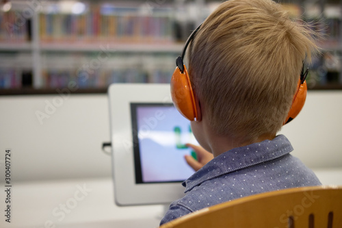 Wallpaper Mural Elementary school boy sitting in library, using touchscreen computer for education. Concept: technology and modern learning environment Torontodigital.ca