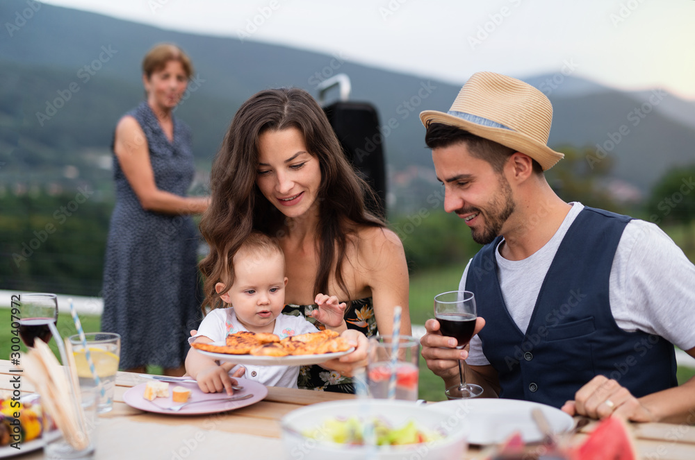 Portrait of family with wine sitting at table outdoors on garden barbecue.