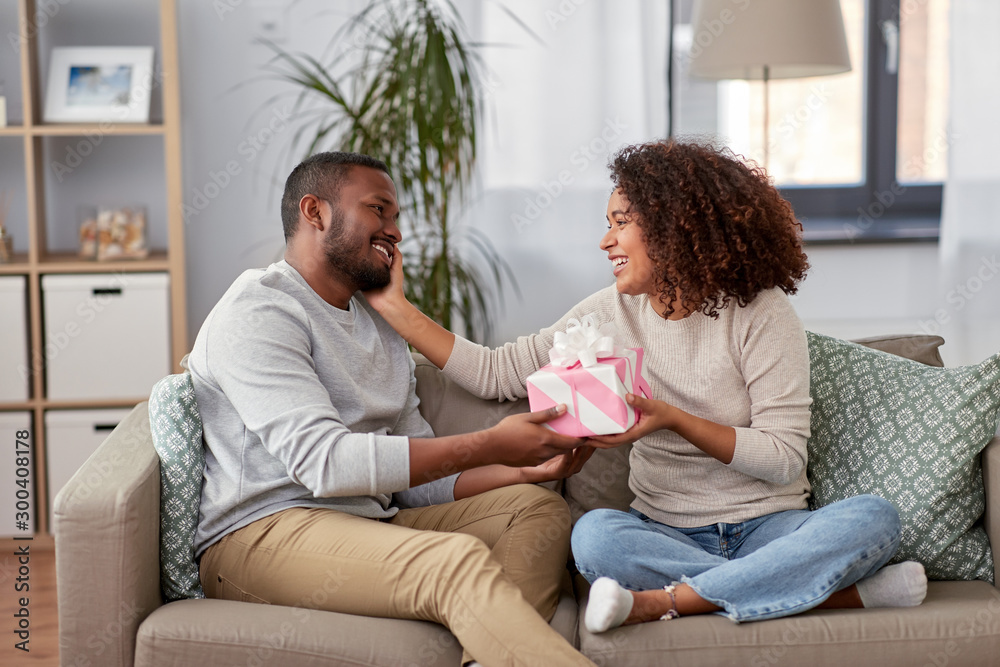 holiday, greeting and people concept - happy african american couple with gift at home