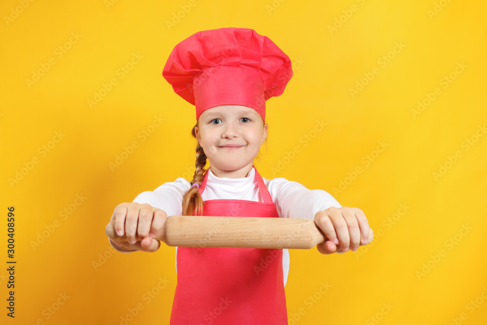 Beautiful little girl chef on a yellow background. The child holds in his hands a wooden rolling pin Beautiful little girl chef on a yellow background. The child holds in his hands a wooden rolling pin