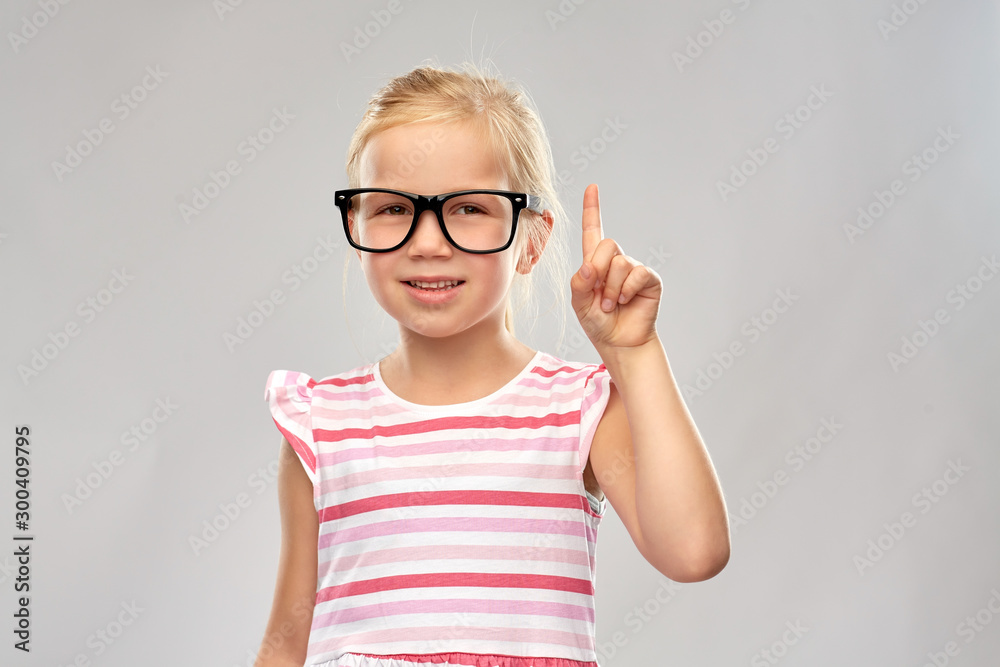 education, school and vision concept - smiling cute little girl in black glasses pointing finger up over grey background