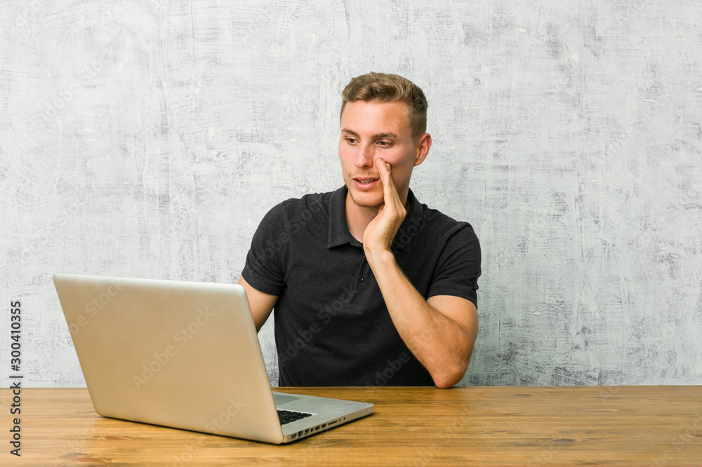 Young entrepreneur working with his laptop on a desk is saying a secret hot braking news and looking aside Young entrepreneur working with his laptop on a desk is saying a secret hot braking news and looking aside