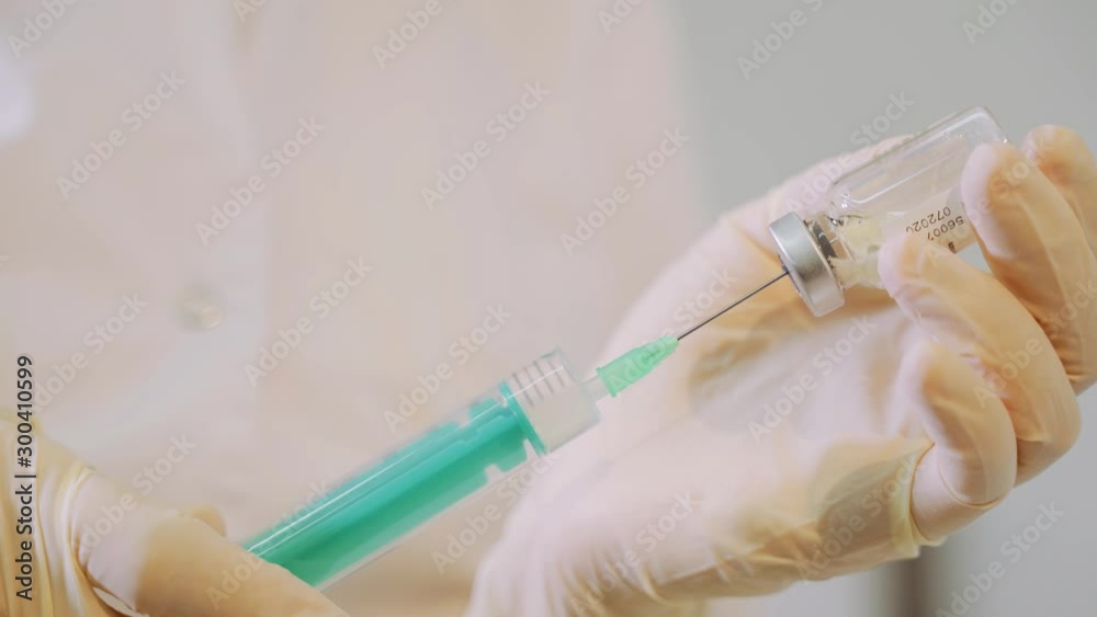 A female nurse prepares an injection syringe, fills a syringe from an ampoule with liquid, provides first aid. Woman's hands in rubber white gloves are injecting into a syringe.