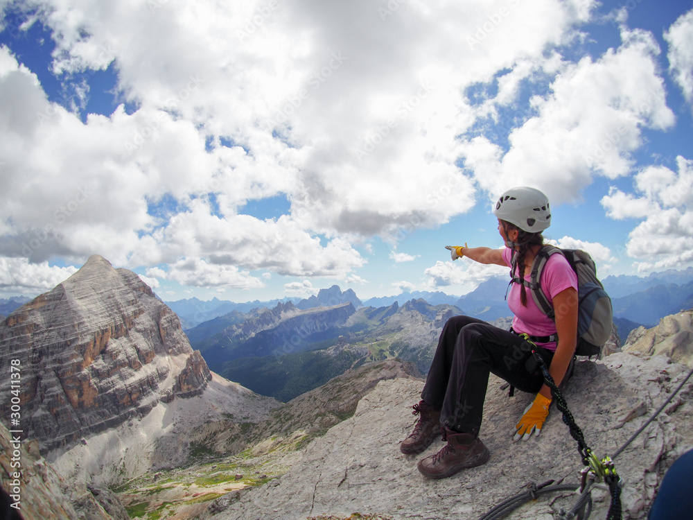 attractive brunette female climber on a mountain peak in the Dolomites pointing to the distance