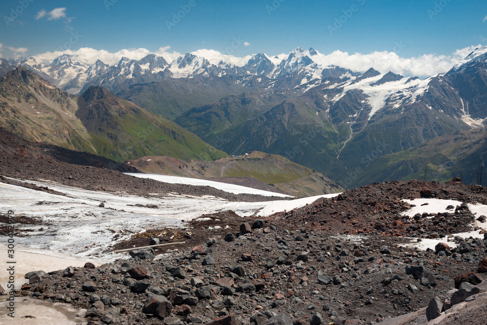 Caucasus mountains near Elbrus volcano with glaciers, clouds, green slopes and peaks.