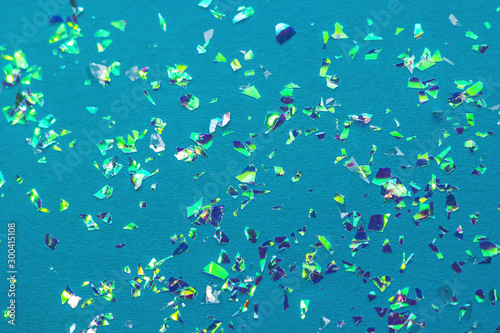 Multicolored holographic confetti on a blue background. © Anna