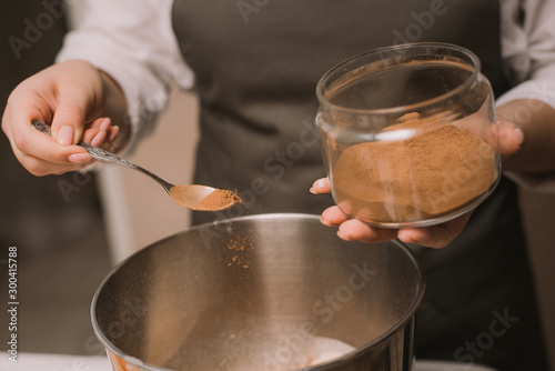 The cook girl pours brown cane sugar into a metal bowl. Cooking sweets in the kitchen.