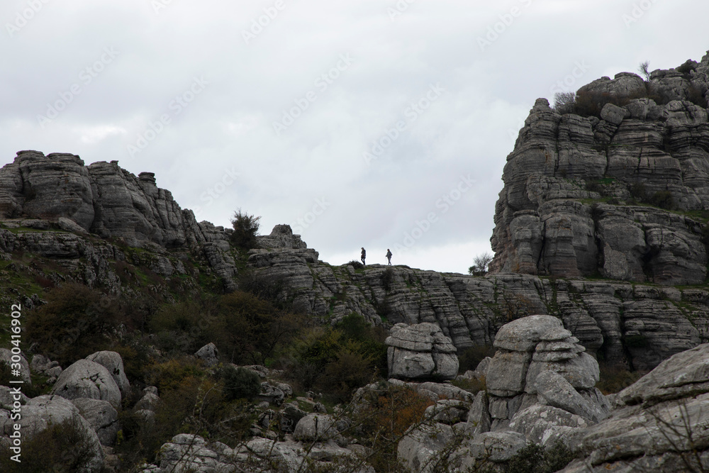 Two people is walking on the patch of a stony mountain 