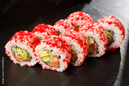 Obraz na płótnie Sushi Rolls with avocado, cucumber and salmon inside on black slate isolated. California rolls covered orange tobiko or masago caviar. Sushi menu. Horizontal photo. w salonie