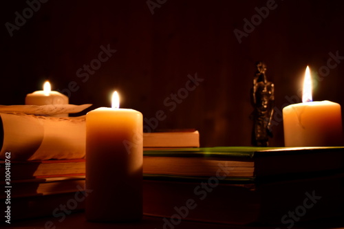 Old books and burning candles on a black background. Ancient manuscripts and a black statue by candlelight.