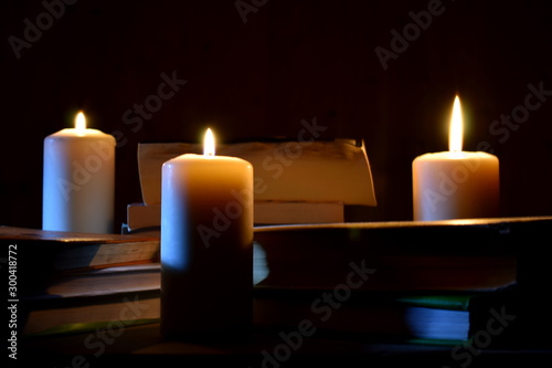 Old books and burning candles on a black background. Ancient manuscripts by candlelight.