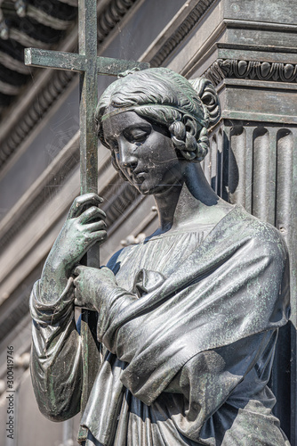 Old metal statue of a sensual woman as a prayer with a cross and covered with spider net in downtown of Dresden, Germany, details, closeup