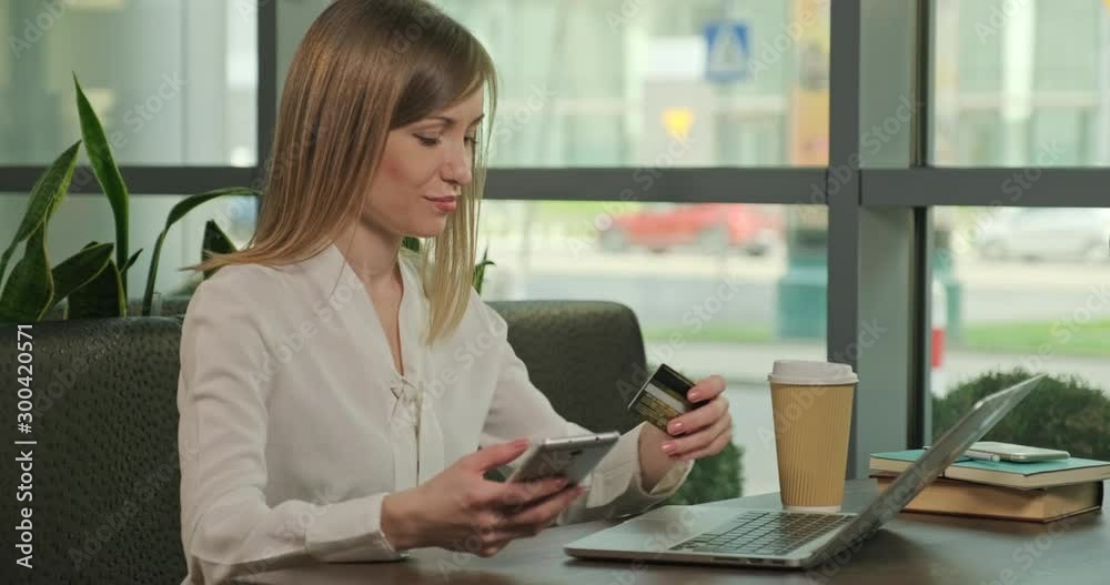 Business woman shopping online with credit card. Female holds in her hand cellphone, sitting at the table cafe. Dolly sho