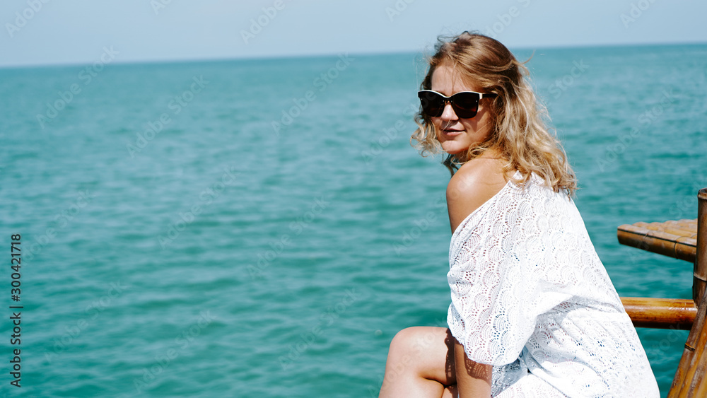Young woman near sea in white dress and sunglasses on an azure background