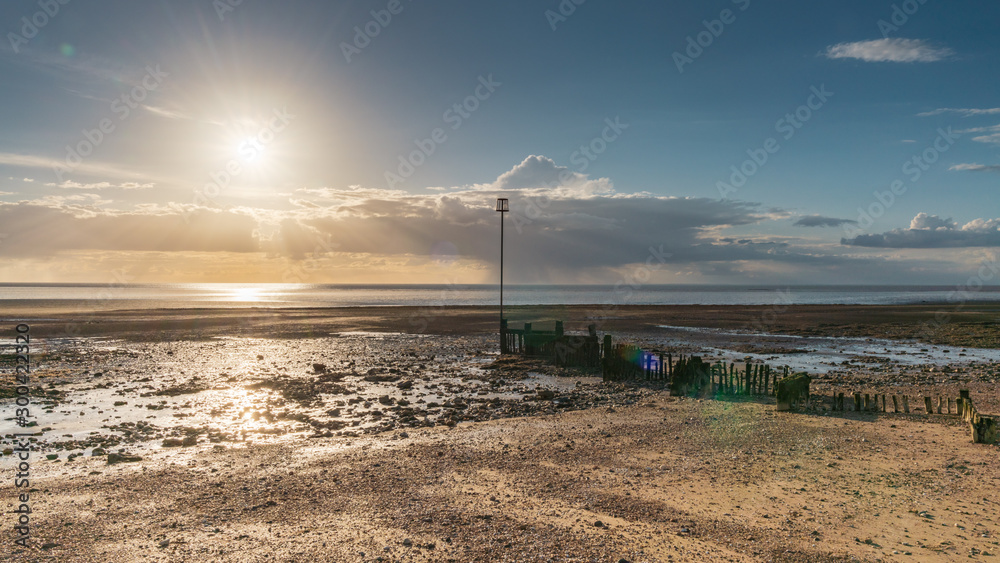 Groynes and the setting sun at the North Beach in Heacham, Norfolk, England, UK