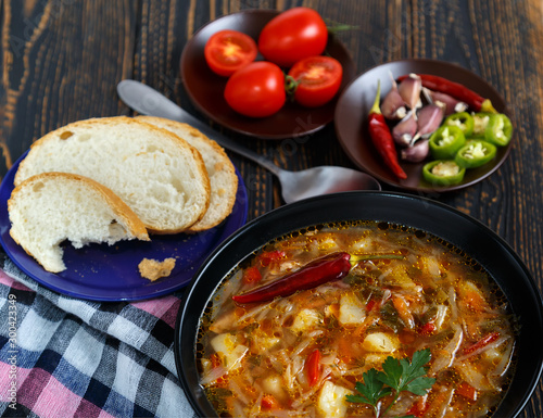 Vegetable soup with tomatoes and chili peppers. Borsch is a national Ukrainian dish. The concept of vegetarian food. Black plate with soup on a black wooden background