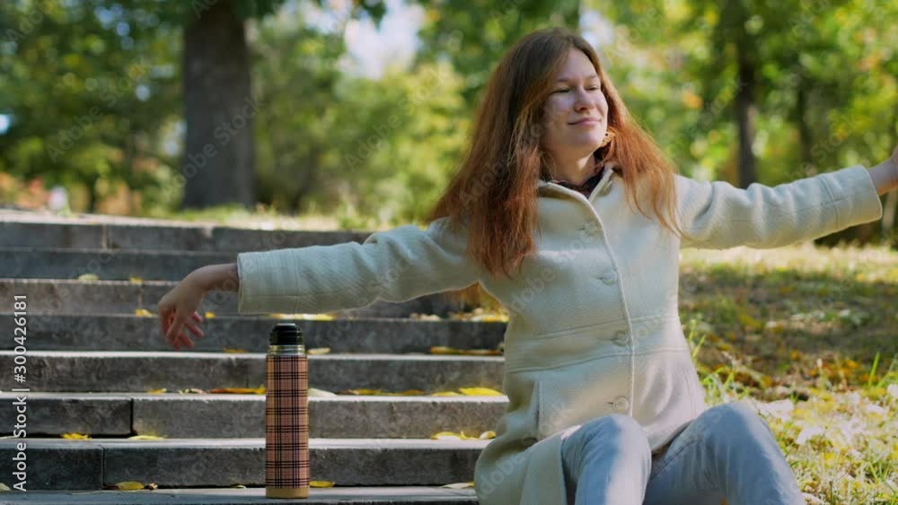 Young girl stretching hands, doing exercises, sitting on stairs in outdoors autumn park, beautiful woman enjoy drinking tea or coffee thermos, lifestyle relax recreation weekend meditation concept Young girl stretching hands, doing exercises, sitting on stairs in outdoors autumn park, beautiful woman enjoy drinking tea or coffee thermos, lifestyle relax recreation weekend meditation concept