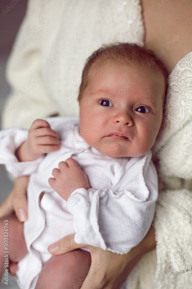 mother in a white robe holds a small newborn daughter against the wall mother in a white robe holds a small newborn daughter against the wall