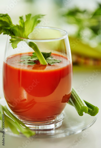 Tomato juice on a white plate with a garnish of celery and parsley. Healthy eating concept.