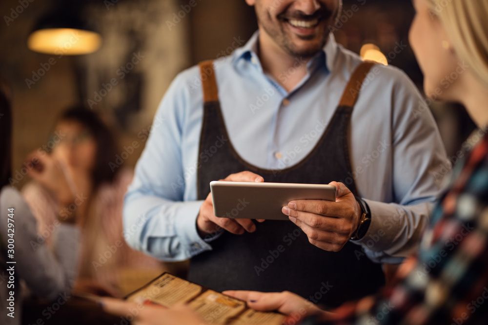 Close-up of waiter using digital tablet while serving a guest in a pub. Close-up of waiter using digital tablet while serving a guest in a pub.