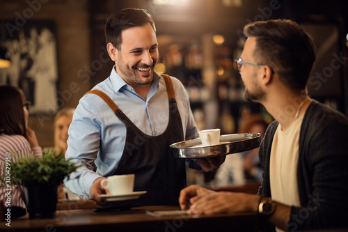 Happy waiter talking to a man while serving him coffee in a cafe. photo