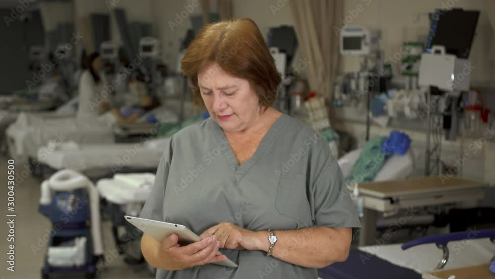 An older nurse using modern technology looks up and smiles at the viewer while holding a tablet computer as she works in a hospital. An older nurse using modern technology looks up and smiles at the viewer while holding a tablet computer as she works in a hospital.