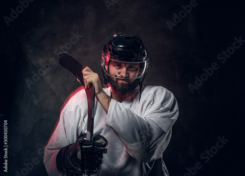 Bearded brutal hockey player is posing for photographer and red light is creating effect of movement.
