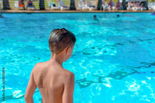 European boy taking off to jump into swimming pool. Back view.