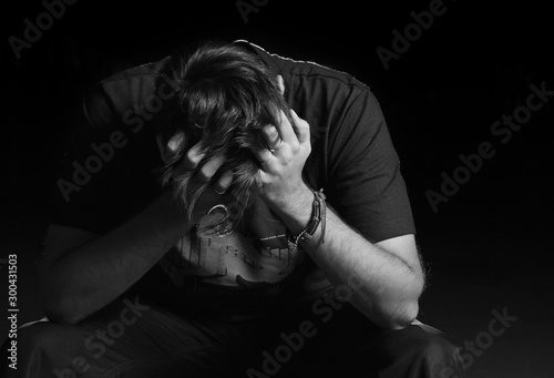 Despair, sadness and loneliness of a person sitting in the dark, crying and covering face with hands. Black and white portrait