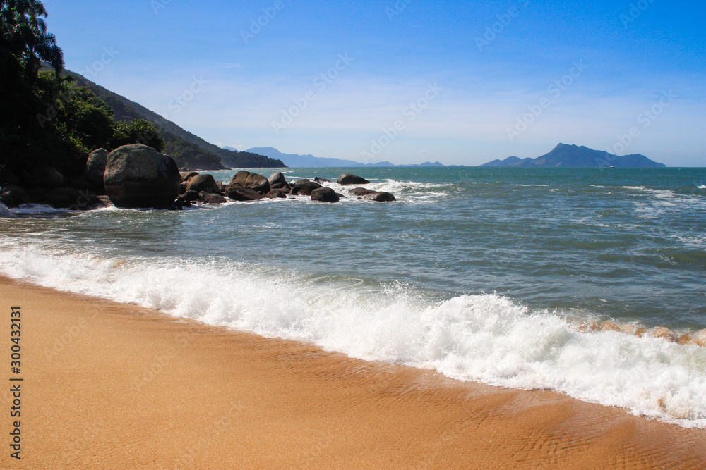 Atlantic ocean with rippling water and sea foam and mountains. Landscape with the beach of Brazil on the island of Ilha Grande.
